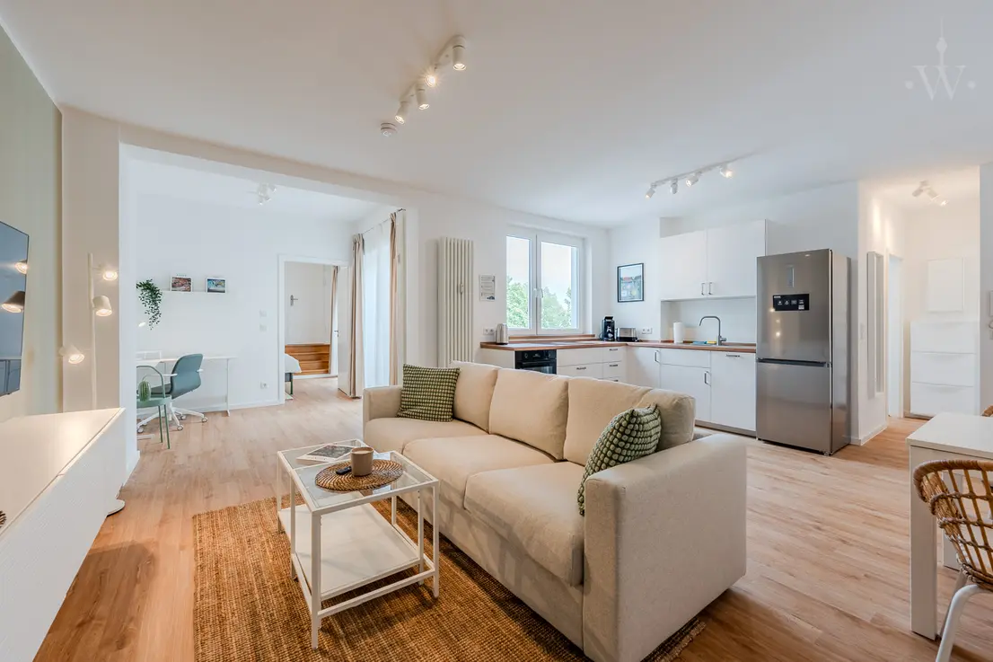 Couch mit kleinem Tisch und Teppich. Außerdem sieht man eine Küche