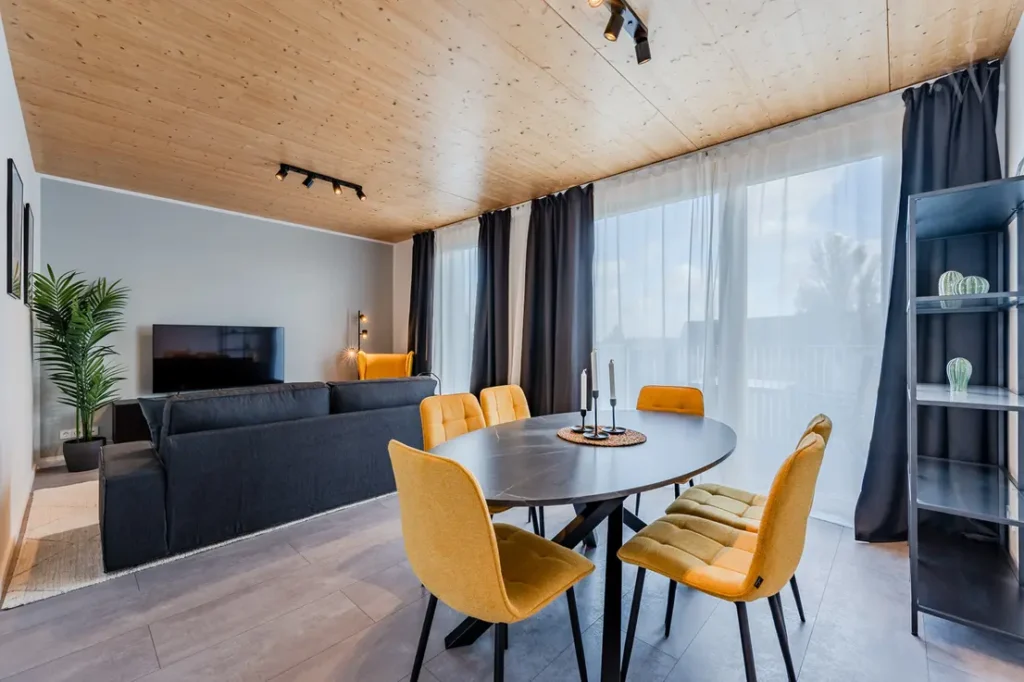 Wohnzimmer mit Esstisch und Stühlen, einer Couch und einem Fernseher sowie einer Pflanze