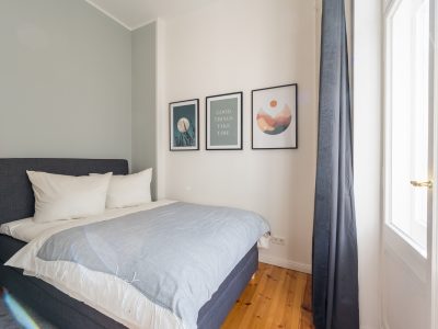 Gemütliches Schlafzimmer mit graublauem Bett, dekorativen Bildern und Vorhängen