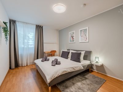 Helles Schlafzimmer mit Doppelbett, Wandbildern und Fenster mit Vorhängen