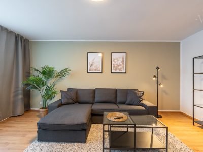 Modernes Wohnzimmer mit schwarzem Ecksofa, Zimmerpflanze und stilvollen Wandbildern